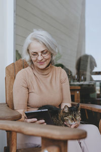 Smiling mature woman using tablet pc with cat on lap at home terrace