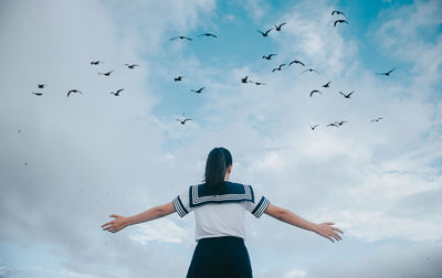 Low angle view of birds flying over teenage girl against cloudy sky