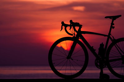 Silhouette bicycle by sea against sky during sunset