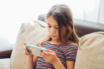 Cute little girl using technology device sitting on sofa. girl playing on phone.