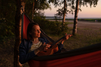 A female travel blogger sits in a hammock and plays the ukulele. hiking and outdoor recreation