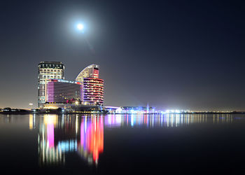 Illuminated building by river against sky at night