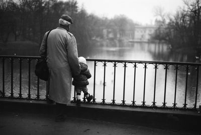 Rear view of man with child standing on bridge over river