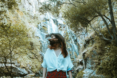 Young woman standing against waterfall