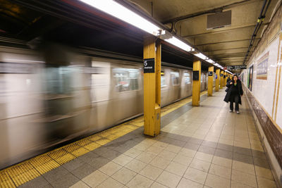 Blurred motion of train by woman walking at railroad station