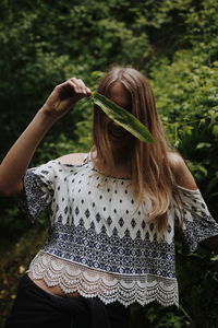 Teenage girl covering face with leaf while standing against plants