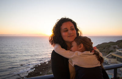 Portrait of mother and daughter against sea during sunset