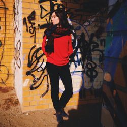 Portrait of young woman standing against graffiti wall