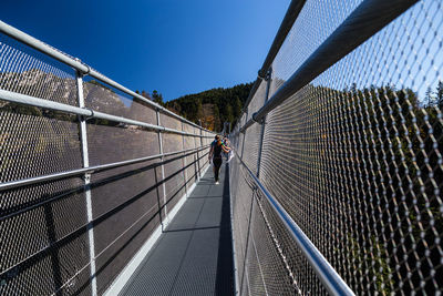 Rear view of man standing on footbridge against clear sky