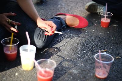 Low section of woman holding cigarette while sitting in front of drinks on street