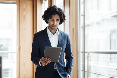 Confident young male entrepreneur with curly black hair using digital tablet at office