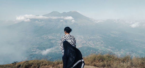 Rear view of man standing on mountain against sky