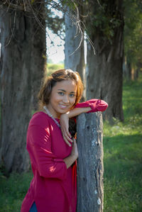 Portrait of smiling young woman standing against tree trunk