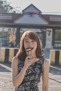 Portrait of young woman eating ice cream while standing in city