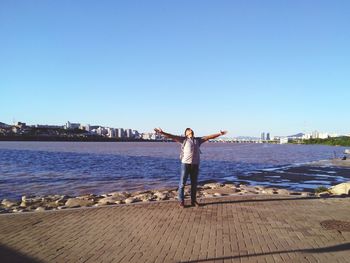 Man with arms outstretched standing at beach against clear sky