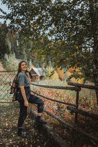 Portrait of smiling young woman standing by tree during autumn