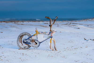 Abandoned broken bicycle on snow covered beach against sky