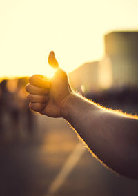 Cropped hand of man gesturing thumbs up during sunset