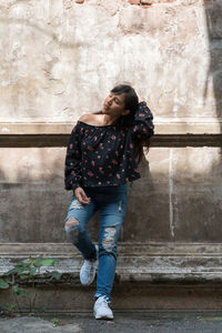 Young woman looking away standing against wall