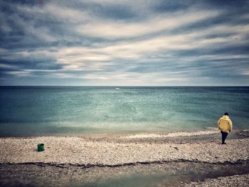 Rear view of woman standing on beach against sky