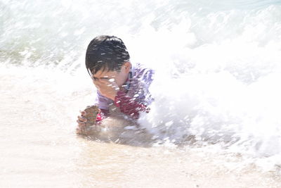 Waves splashing on boy lying in sea