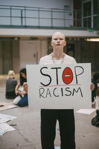 Young female activist with stop racism poster standing in building