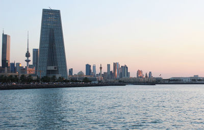 Sea by cityscape against clear sky during sunset