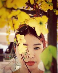 Close-up portrait of young woman standing by yellow flowers on twigs