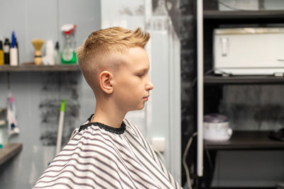 A blond boy is sitting in a barbershop, getting his hair done