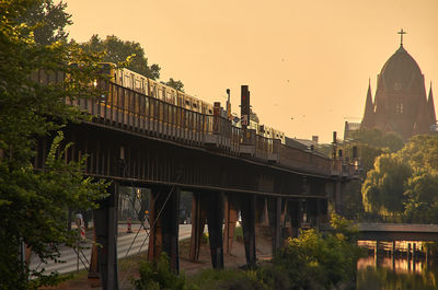 Bridge amidst trees and buildings against sky during sunset