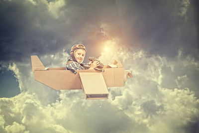 Low angle portrait of boy flying airplane against cloudy sky