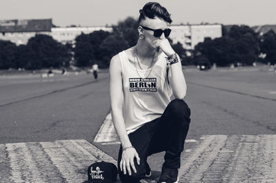 Young woman wearing sunglasses while kneeling on road