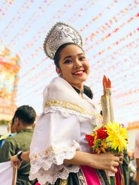 Low angle portrait of smiling woman holding flowers and artificial candles at temple