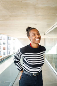 Cheerful african american female in casual wear looking at camera with smile while standing on balcony of building on summer day