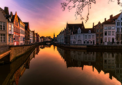 Reflection of buildings on canal in city during sunset