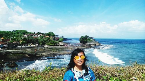 Portrait of woman wearing sunglasses while standing by sea against cloudy sky at uluwatu temple