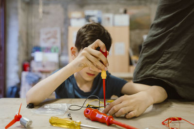 Boy learning to repair electrical component using screwdriver at workshop in school