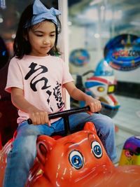 Portrait of smiling young girl sitting on a static toy car