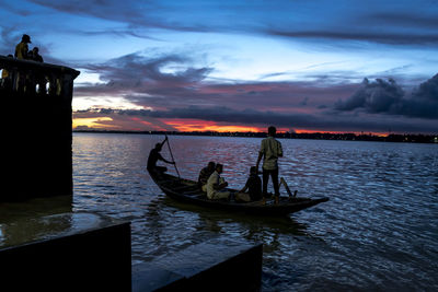 Men standing on boat in sea against sky during sunset