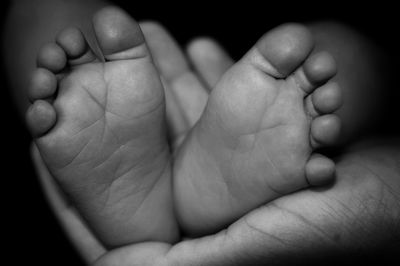 Cropped image of hand holding baby leg against black background