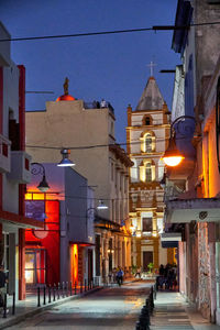 Illuminated street amidst buildings in city at dusk