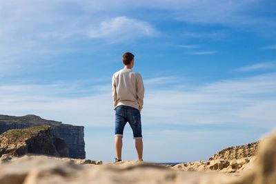 Rear view of man standing on rock against sky