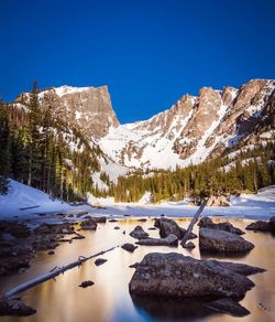 Scenic view of frozen lake by mountains against clear blue sky