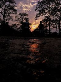 Silhouette trees on field against orange sky