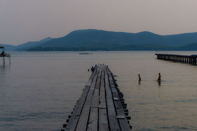 People on pier by sea against sky