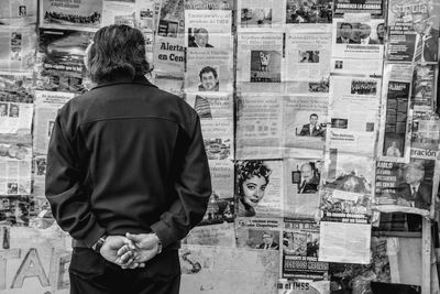 Rear view of man standing against newspapers on wall