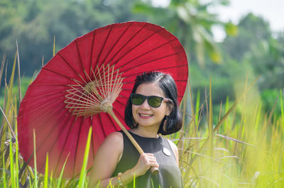 Smiling young woman with red umbrella on field