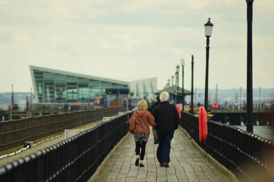 Rear view of senior man and woman walking on bridge against sky