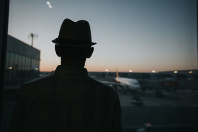 Rear view of silhouette man in city against sky during sunset