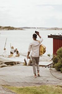 Rear view of man waving at friends sitting on jetty during picnic at harbor